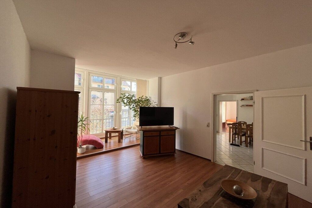 Un salon spacieux avec un téléviseur à écran plat posé sur un meuble en bois, une grande fenêtre offrant une belle vue et une porte donnant sur une autre pièce.