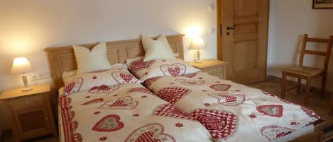 Una cama con una colcha estampada, dos lámparas de noche, una puerta de madera y una silla.
