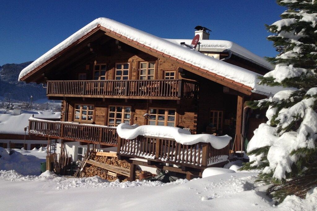 A wooden chalet with a balcony, surrounded by snow-covered mountains.