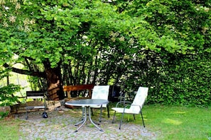 An outdoor seating area with a table and chairs, surrounded by lush greenery and a tree. - Holiday home in Kinding with swimming pool (Kinding)