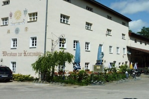 Un bâtiment sur lequel on peut lire l’inscription « Wirtshaus zur Kratzmühle » et devant lequel se trouve une statue.