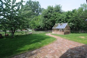 A brick pathway leading to a wooden structure with a glass roof, surrounded by lush greenery and trees. - Holiday home with 2 bedrooms (Wunstorf-Idensen)