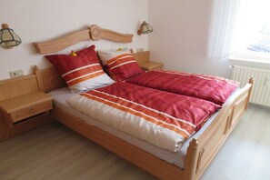 Een tweepersoonsbed met houten frame, twee nachtkastjes en een bijzettafeltje.