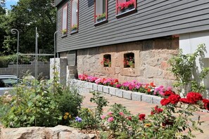 Un bâtiment doté d’une façade en pierre, de fenêtres à cadre rouge et d’un parterre fleuri où poussent différentes variétés de fleurs aux couleurs vives.