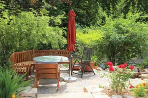 Un patio esterno con tavolo e sedie di legno, un ombrellone rosso e una vasca idromassaggio.