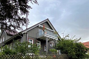 Una casa a due piani con un balcone, una recinzione in legno e un tetto con tegole rosse.