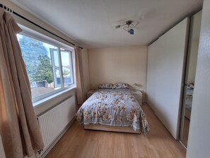 Ein Schlafzimmer mit einem Bett, einem Heizkörper, einem Fenster mit Vorhängen und einem Deckenventilator.