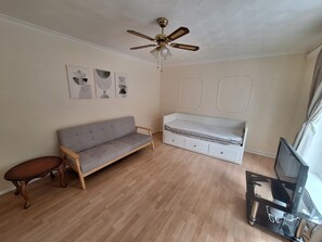 A room with a grey sofa, a bed with storage drawers, a ceiling fan, and a television on a stand. - 3BR Home w/ Driveway Parking Near Cardiff Centre (London)