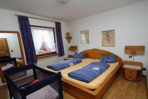 A bedroom with two beds, a wooden headboard, a nightstand, a small table, and a window with curtains. - Holiday apartment with 1 bedroom (Zell \/ Mosel)