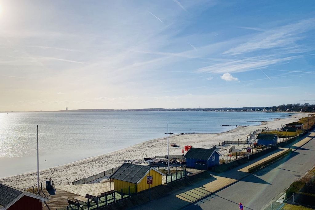 Eine Küstenstraße mit Gebäuden am Strand, einem Steg und freiem Blick auf das Meer.