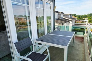 Ein Balkon mit Tisch und Stühlen, großen Fenstern und Blick auf die Nachbarschaft.