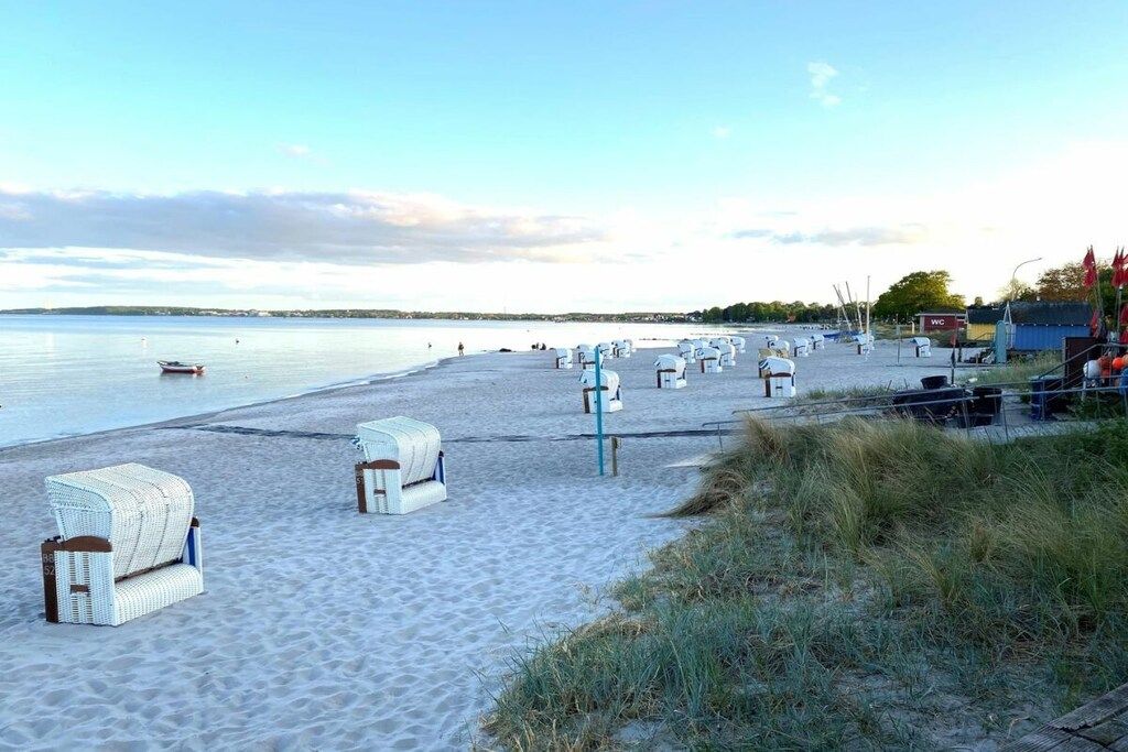 Une plage avec des chaises en osier blanches et un petit bâtiment sur lequel est affiché un panneau indiquant « toilettes ».