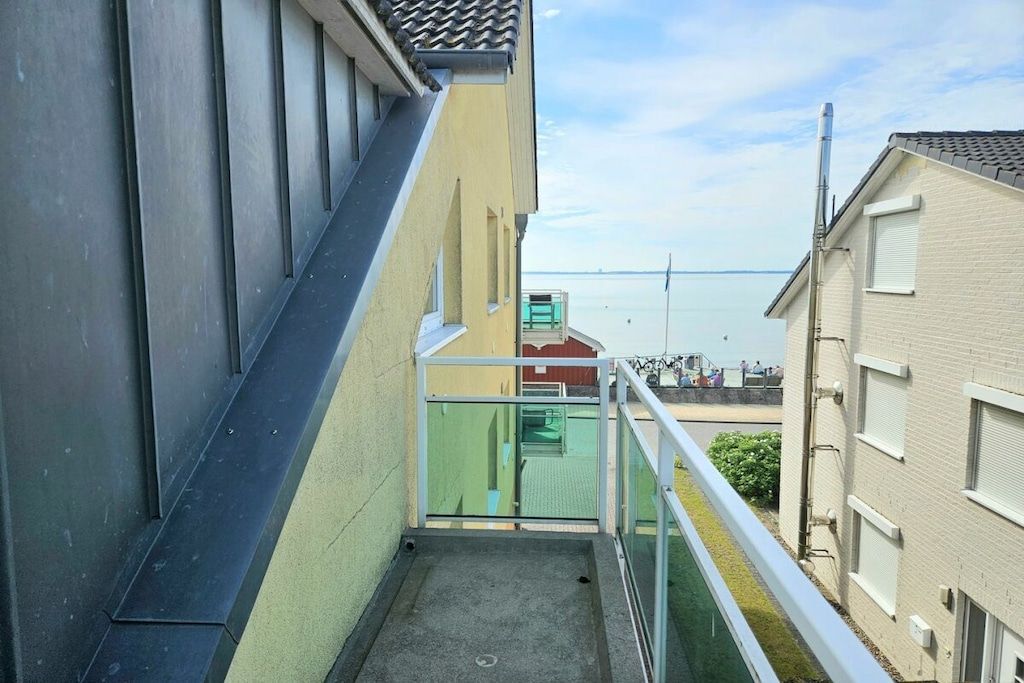 A narrow outdoor corridor with a glass railing, leading to a building with a tiled roof.