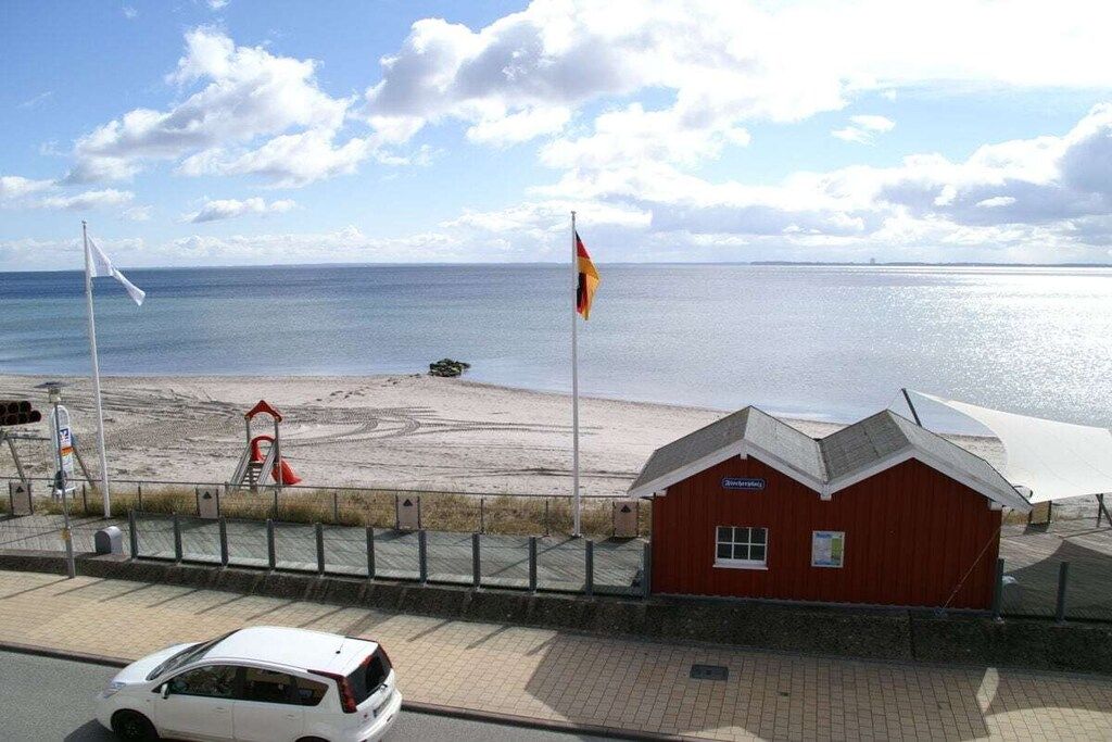 A coastal road with a beach, a lifeguard tower, and a red building with a white awning.