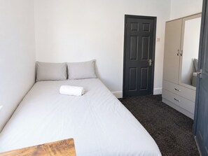 Ein Schlafzimmer mit einem Bett, einer dunklen Tür, einem Kleiderschrank und einem Spiegel.
