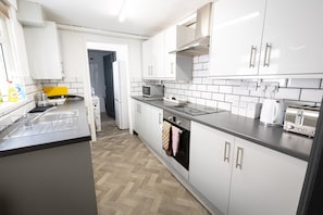 A modern kitchen with white cabinets, a microwave, a kettle, and a toaster. - Central 4-BR Middlesbrough | Walk to Station & Uni (Middlesbrough)