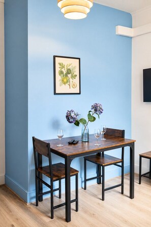 A dining area with a blue wall, a framed botanical print, a vase with flowers, and a table with chairs. - Central 4-BR Middlesbrough | Walk to Station & Uni (Middlesbrough)