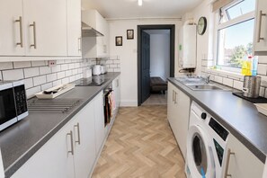 A modern kitchen with a microwave, oven, sink, and washing machine. - Central 4-BR Middlesbrough | Walk to Station & Uni (Middlesbrough)