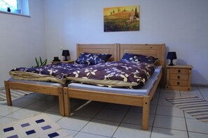 A double bed with a wooden frame, two bedside tables with lamps, a wall-mounted painting, and a patterned rug on a tiled floor.