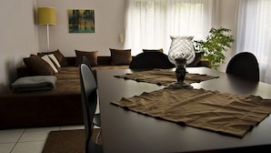 A living room with a sofa, a dining table with placemats, a lamp, and a painting on the wall. - Holiday apartment with 1 bedroom (Eschweiler)