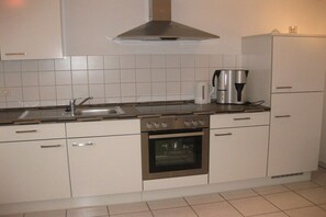 A kitchen with white cabinets, a stainless steel range hood, a coffee maker, and an oven.