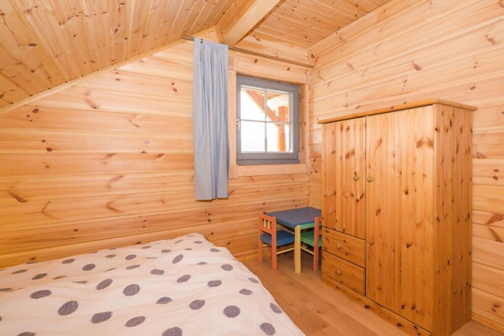 Een kleine kamer met houten wanden, een bed, een bureau en een kledingkast.
