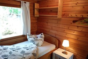 A wooden cabin room with a bed, a bedside lamp, and a window with curtains. - Heide log cabin "Blueberry" (Neuenkirchen)