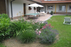 Un espace patio aménagé avec une table et des chaises, entouré d’un jardin où poussent différentes plantes et fleurs.