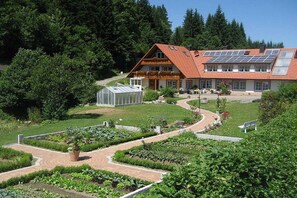 A building with a red roof, solar panels, and a garden with a greenhouse. - Hetzlenmühle 3-room apartment no. 2 (Görwihl)