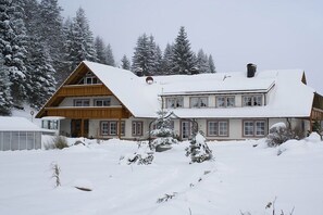 Un chalet à deux étages, doté d’un toit à forte pente, entouré d’arbres couverts de neige.