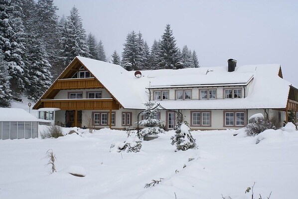 A two-story chalet with a steeply pitched roof, surrounded by snow-covered trees. - Hetzlenmühle 3-room apartment no. 2 (Görwihl)