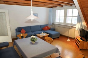 Une pièce chaleureuse avec un canapé bleu, une petite table sur laquelle est posé un vase, et un téléviseur sur un meuble en bois.