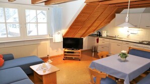 Tunnelmallinen, avoimen pohjaratkaisun huone, jossa on televisio, ruokapöytä ja siniset sohvat.