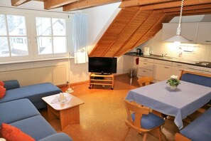 A cozy loft-style room with a TV, dining table, and blue sofas. - Hetzlenmühle 3-room apartment no. 2 (Görwihl)