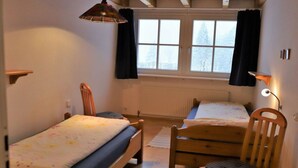 Makuuhuoneessa on kaksi puista sänkyä, tuoli, ikkuna, jossa on verhot, ja patteri.