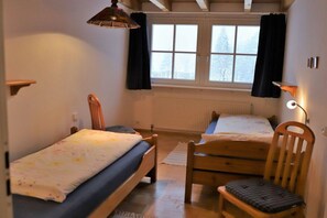 A bedroom with two wooden beds, a chair, a window with curtains, and a radiator. - Hetzlenmühle 3-room apartment no. 2 (Görwihl)