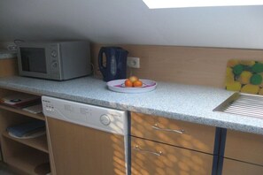A compact kitchen with a microwave, kettle, and a bowl of fruit on the counter. - in the Elderberry Grove house (Wesel)