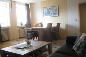 A living room with a dining table, chairs, a sofa, a coffee table, and a painting on the wall. - in the Elderberry Grove house (Wesel)