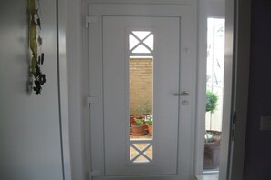 A white door with a window, a brick wall, and potted plants visible through the window. - in the Elderberry Grove house (Wesel)