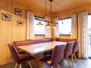 Un intérieur en bois avec une longue table à manger, des chaises rembourrées et un luminaire suspendu.