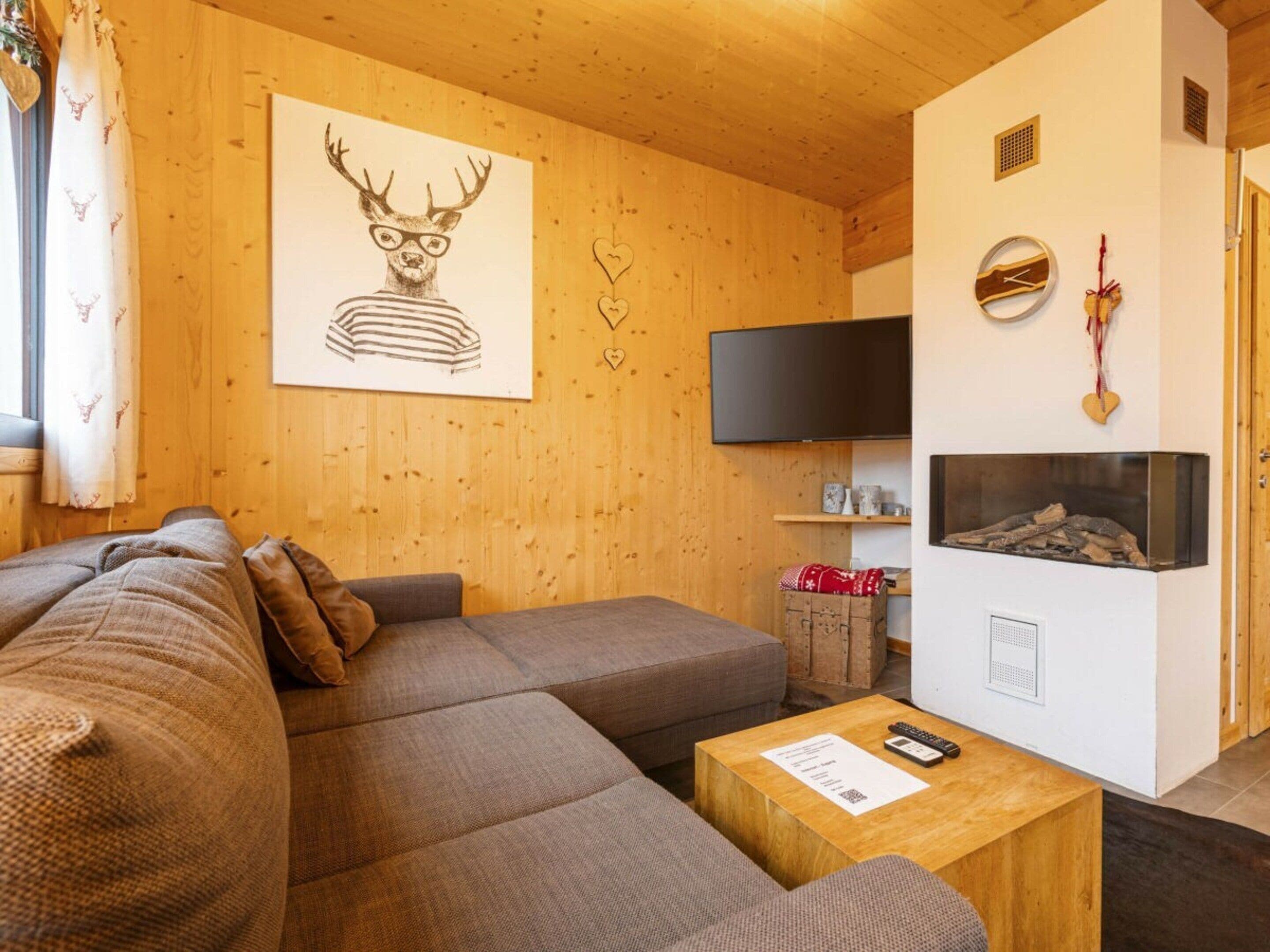 A cozy living room with a sofa, a flat-screen TV, a fireplace, and a wooden wall.