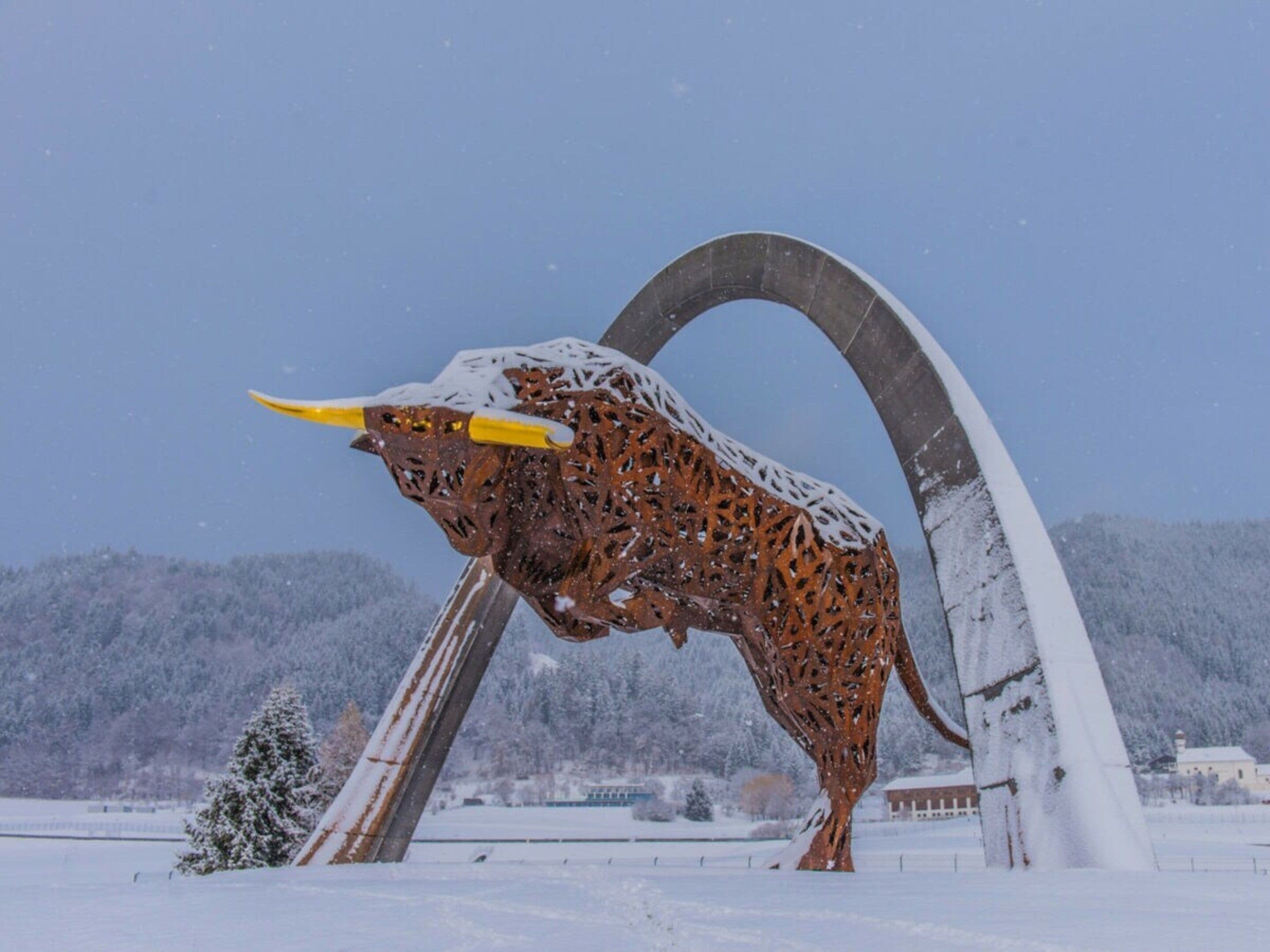 Metallinen härkäpatsas lumisessa maisemassa, taivaalla ei ole pilviä.