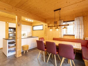 A wooden interior with a dining area, kitchen, and a window with curtains. - Cabin in Hohentauern With Sauna (Hohentauern)
