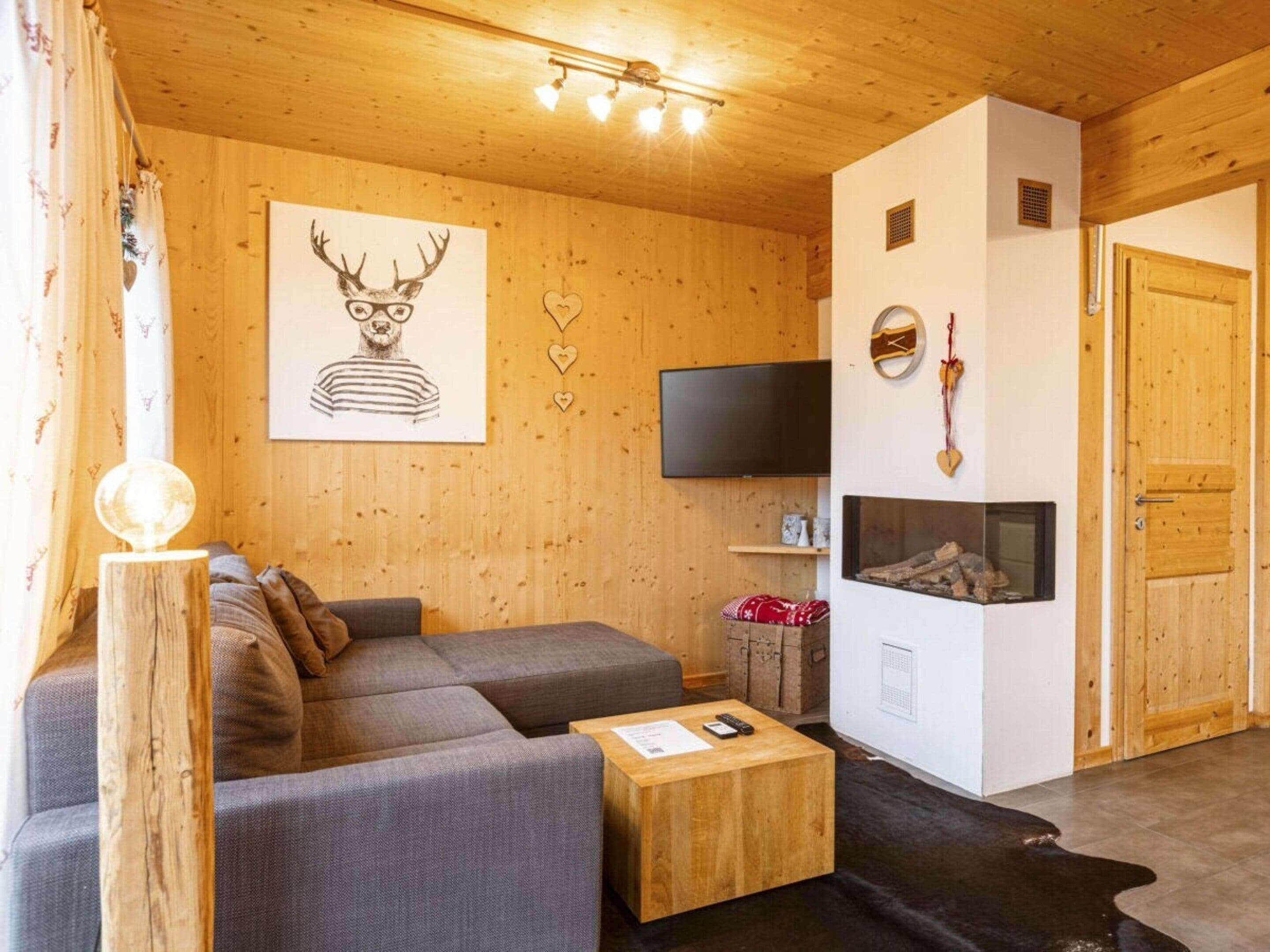 Un salon chaleureux avec un canapé d’angle, une table basse en bois, une cheminée et un téléviseur fixé au mur.