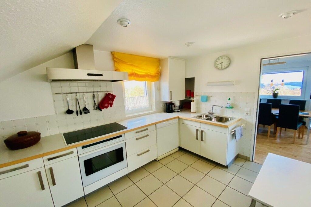A kitchen with white cabinets, a stove, a sink, and a window with yellow curtains.