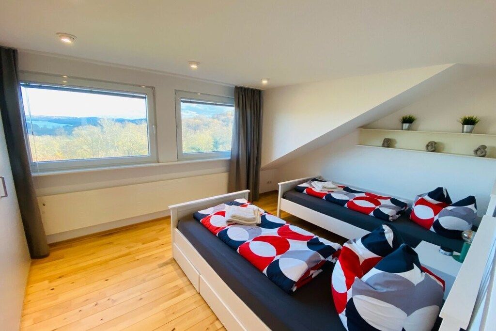 A bedroom with two beds, large windows, a sloped ceiling, and a small shelf with plants.
