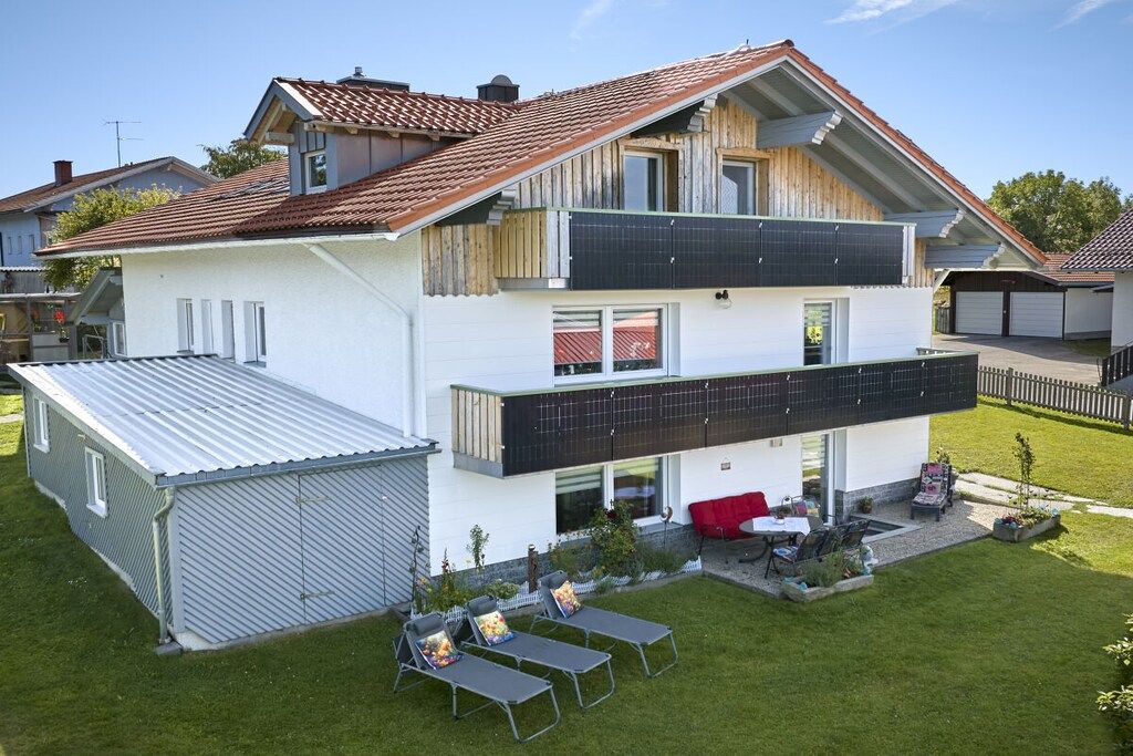 Ett tvåvåningshus med ett platt tak, en balkong och ett litet garage som är sammanbyggt med huset.