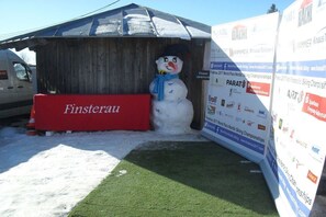 Une sculpture de bonhomme de neige se trouve à côté d’une structure en bois sur laquelle est apposée une pancarte rouge portant l’inscription « Finsterau ».