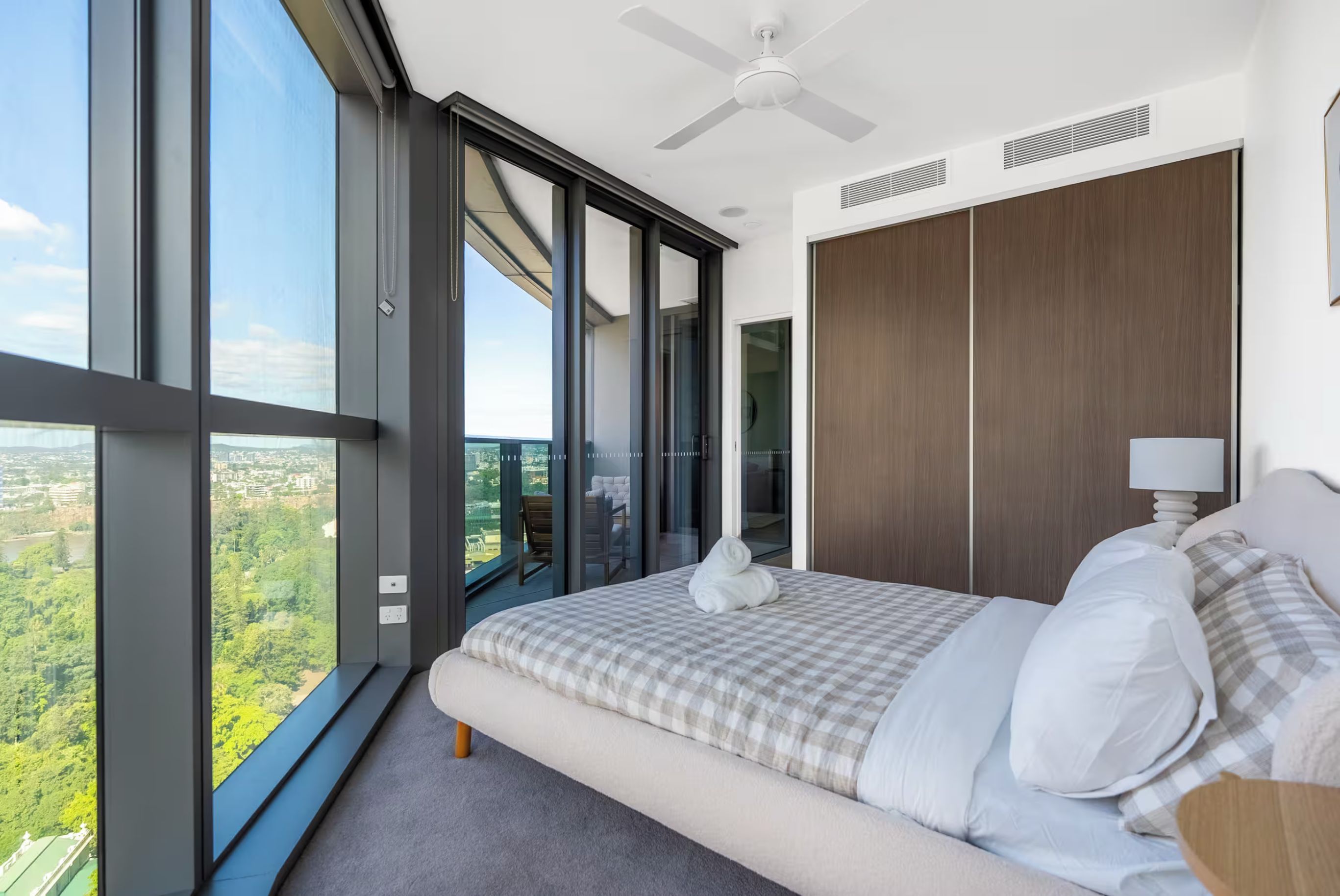 A bedroom with a large window, a bed, a ceiling fan, and a view of a cityscape.