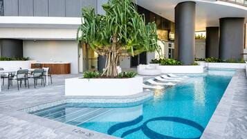 A modern indoor pool area with a large tree, seating, and a clear depth marker.